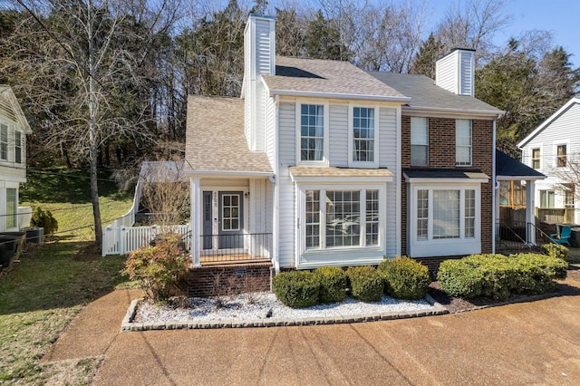 view of front of house featuring brick siding, a chimney, fence, and roof with shingles