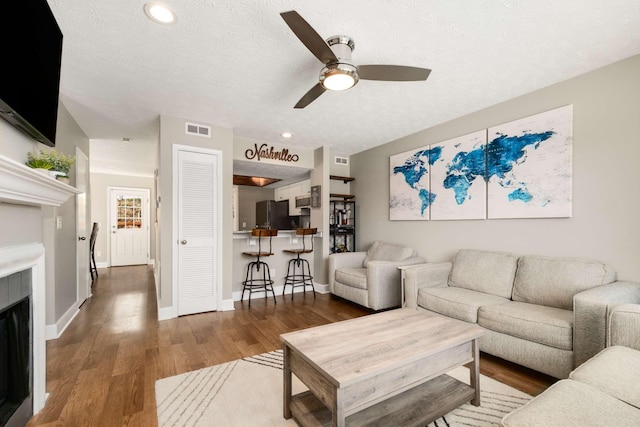 living room featuring baseboards, visible vents, wood finished floors, a textured ceiling, and a fireplace