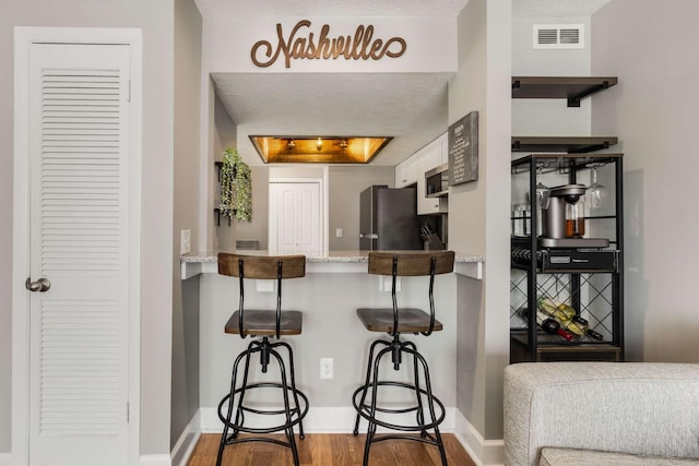 kitchen featuring visible vents, appliances with stainless steel finishes, a kitchen breakfast bar, wood finished floors, and a peninsula