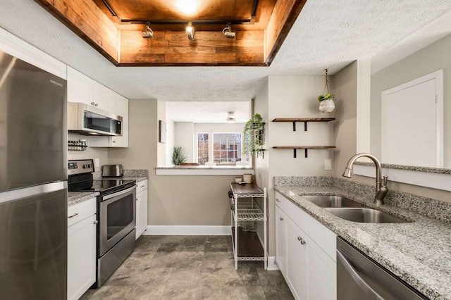 kitchen featuring white cabinets, light stone counters, appliances with stainless steel finishes, a textured ceiling, and a sink