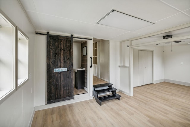 unfurnished living room featuring a ceiling fan, wood finished floors, baseboards, and a barn door