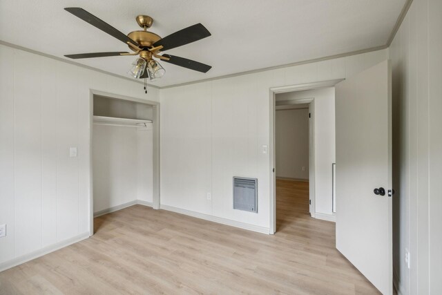 unfurnished bedroom with a ceiling fan, ornamental molding, heating unit, light wood-type flooring, and a closet