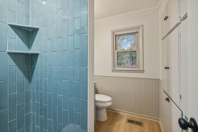 bathroom featuring a wainscoted wall, crown molding, visible vents, toilet, and wood finished floors