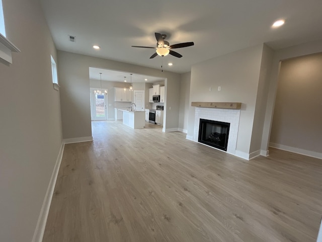 unfurnished living room featuring light wood finished floors, a tiled fireplace, a ceiling fan, a sink, and baseboards