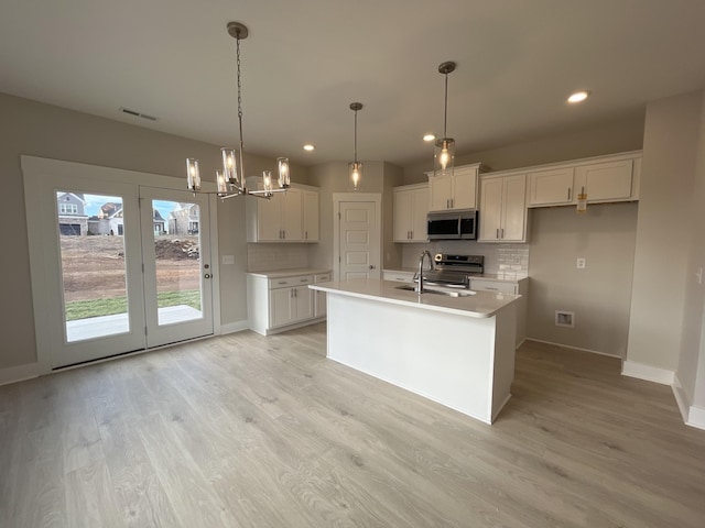 kitchen featuring a kitchen island with sink, stainless steel appliances, a sink, white cabinetry, and light countertops