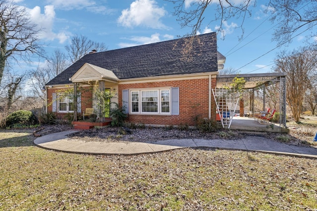 new england style home featuring brick siding, roof with shingles, a chimney, and a front lawn