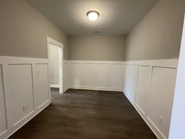 corridor with dark wood finished floors, visible vents, and a decorative wall