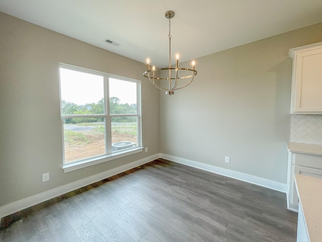 unfurnished dining area featuring a chandelier, dark wood-type flooring, visible vents, and baseboards