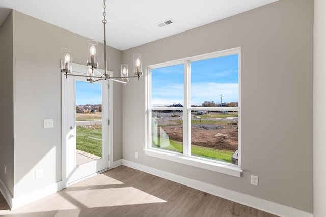 unfurnished dining area with baseboards, visible vents, a chandelier, and wood finished floors