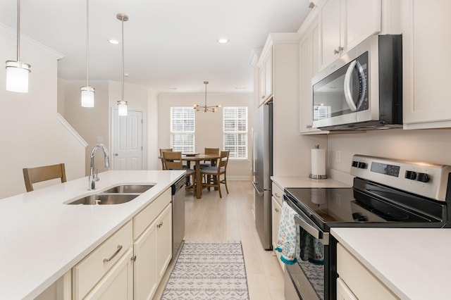 kitchen with appliances with stainless steel finishes, light countertops, a sink, and decorative light fixtures