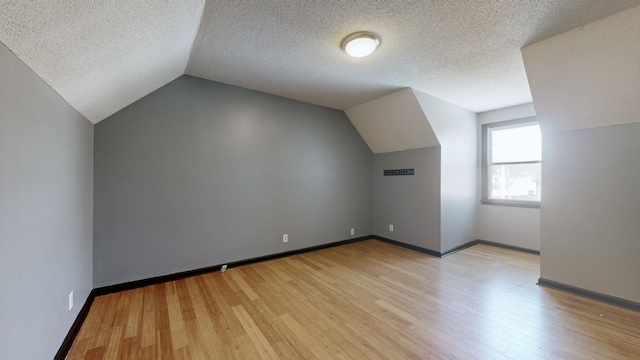 additional living space featuring light wood-type flooring, baseboards, vaulted ceiling, and a textured ceiling