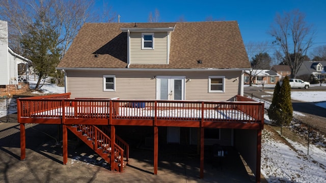 snow covered house featuring stairs, french doors, a shingled roof, and a wooden deck