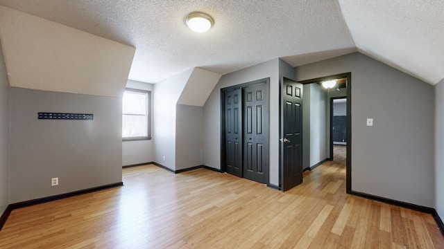 bonus room featuring vaulted ceiling, a textured ceiling, light wood-type flooring, and baseboards