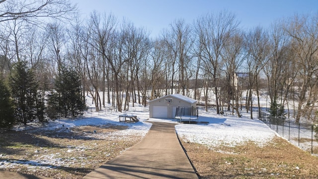 yard layered in snow with a garage, a trampoline, and fence