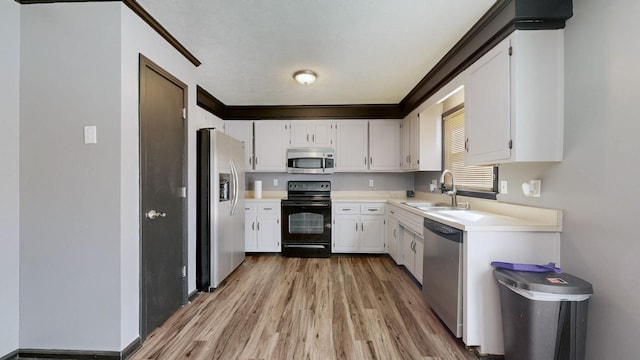 kitchen with light wood finished floors, white cabinets, stainless steel appliances, light countertops, and a sink