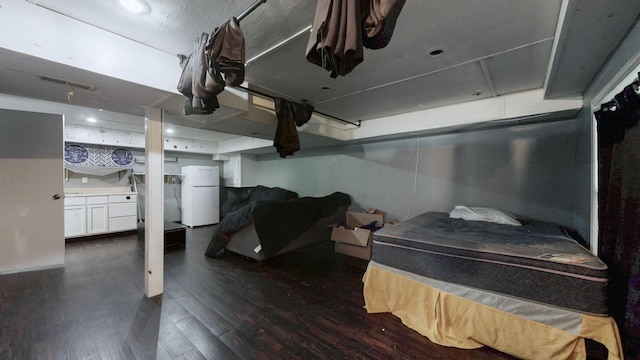 finished basement featuring visible vents, dark wood finished floors, and freestanding refrigerator