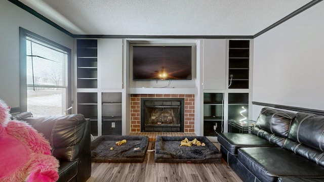 living room with built in shelves, a brick fireplace, a textured ceiling, and wood finished floors