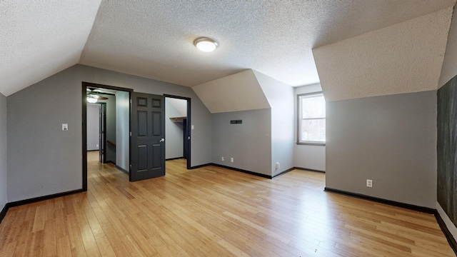 additional living space featuring light wood-style flooring, baseboards, vaulted ceiling, and a textured ceiling