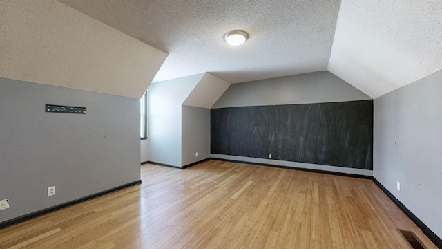 additional living space featuring lofted ceiling, light wood finished floors, a textured ceiling, and baseboards