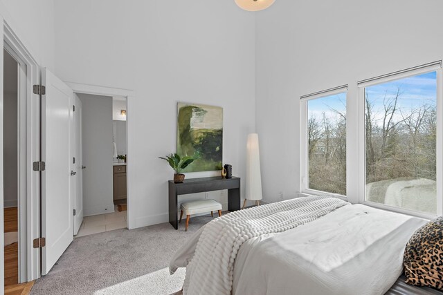 bedroom featuring a towering ceiling, baseboards, ensuite bathroom, and light colored carpet