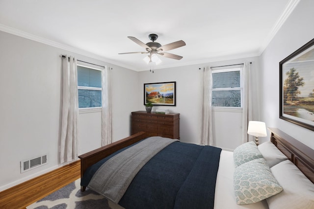 bedroom with multiple windows, visible vents, wood finished floors, and ornamental molding