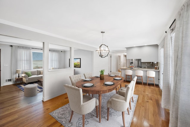 dining area featuring crown molding, light wood-type flooring, and an inviting chandelier