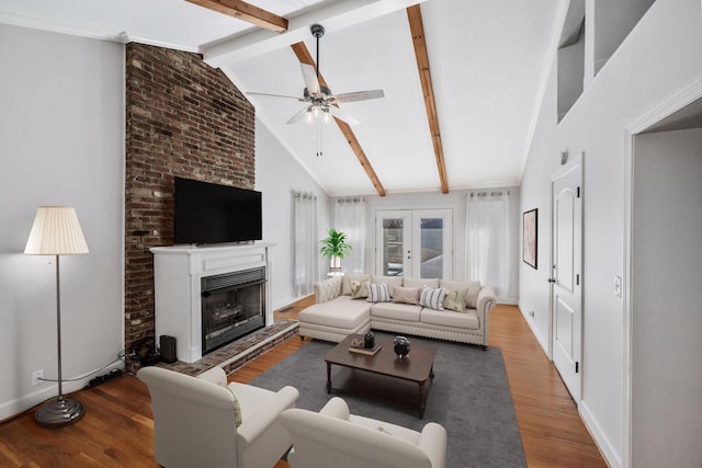 living room with vaulted ceiling with beams, ceiling fan, a fireplace with raised hearth, wood finished floors, and french doors