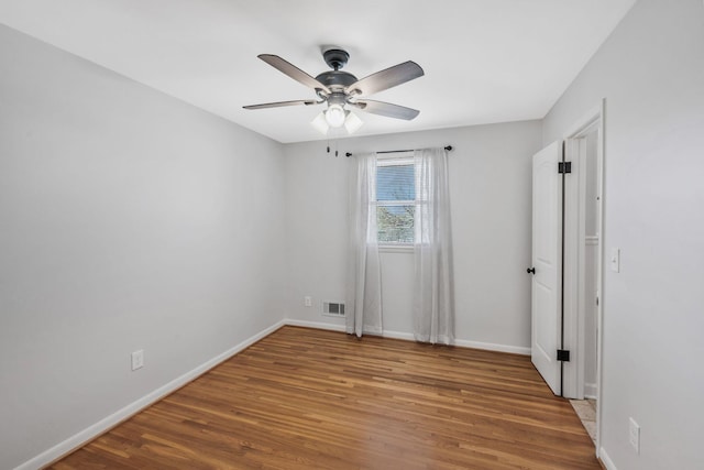 empty room featuring ceiling fan, wood finished floors, visible vents, and baseboards