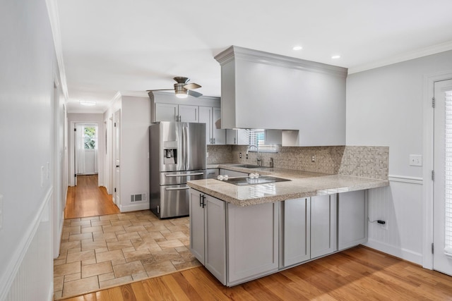 kitchen featuring crown molding, stainless steel refrigerator with ice dispenser, light countertops, a sink, and a peninsula