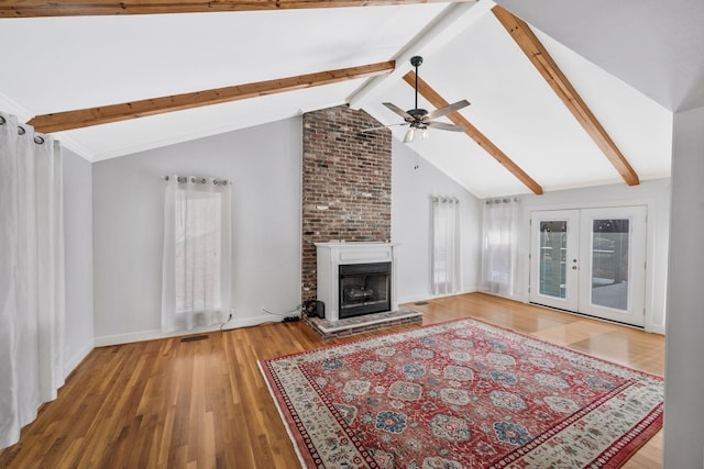 unfurnished living room with a large fireplace, ceiling fan, wood finished floors, vaulted ceiling with beams, and french doors