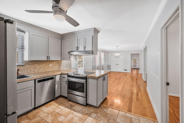 kitchen with under cabinet range hood, gray cabinetry, a peninsula, appliances with stainless steel finishes, and decorative backsplash