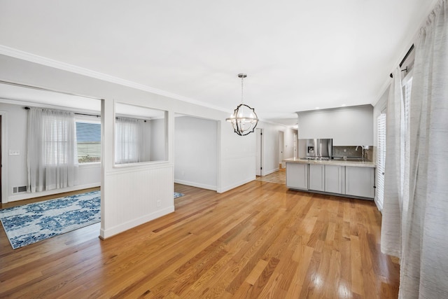 kitchen with pendant lighting, crown molding, stainless steel refrigerator with ice dispenser, light countertops, and a chandelier