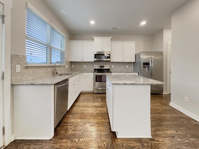 kitchen featuring appliances with stainless steel finishes, light stone counters, a center island, white cabinetry, and a sink