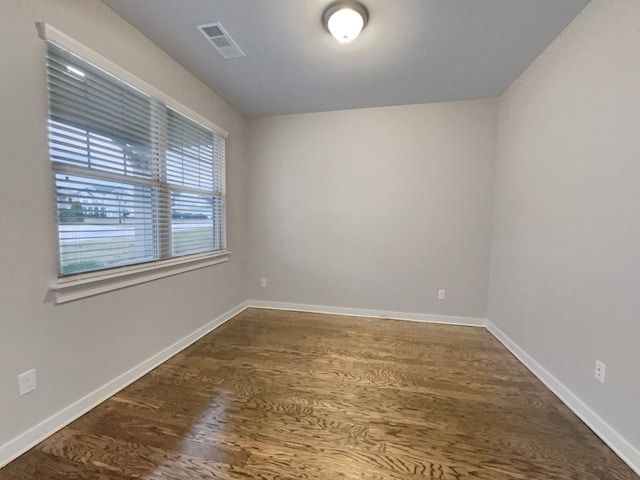 empty room featuring dark wood finished floors, visible vents, and baseboards