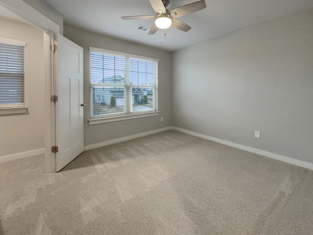 spare room with a ceiling fan, light colored carpet, visible vents, and baseboards