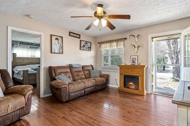 living area featuring a ceiling fan, dark wood finished floors, a textured ceiling, and a glass covered fireplace