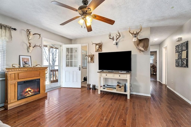 unfurnished living room featuring dark wood-type flooring, a glass covered fireplace, ceiling fan, a textured ceiling, and baseboards