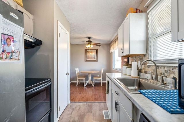 kitchen with under cabinet range hood, white cabinetry, light countertops, freestanding refrigerator, and black electric range oven