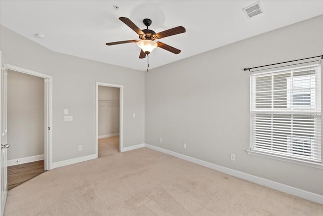 unfurnished bedroom with light colored carpet, a walk in closet, visible vents, and baseboards