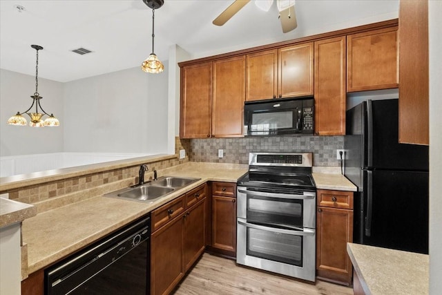 kitchen featuring hanging light fixtures, black appliances, light countertops, and a sink