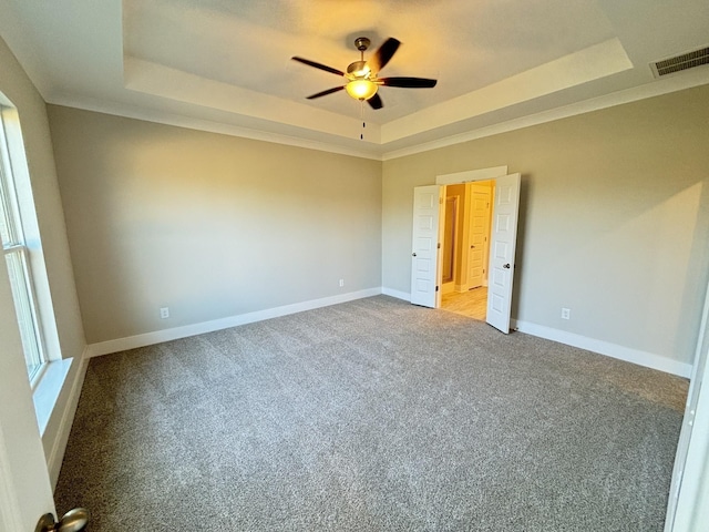 unfurnished bedroom with a tray ceiling, carpet flooring, visible vents, and baseboards