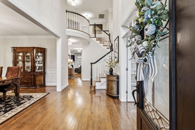 foyer entrance featuring visible vents, wood finished floors, a high ceiling, stairs, and crown molding