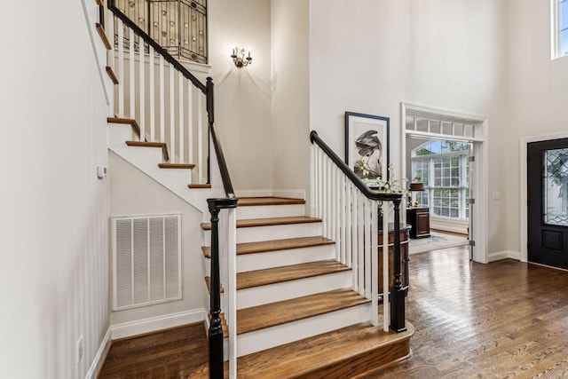 entrance foyer featuring baseboards, visible vents, a towering ceiling, dark wood-style floors, and stairway