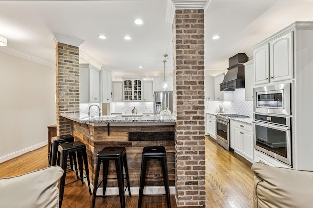 kitchen featuring stainless steel appliances, light stone counters, a peninsula, and custom exhaust hood