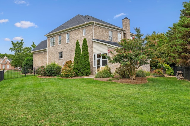 back of house featuring a chimney, fence, a lawn, and brick siding