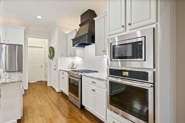 kitchen with light stone counters, tasteful backsplash, custom range hood, appliances with stainless steel finishes, and white cabinets