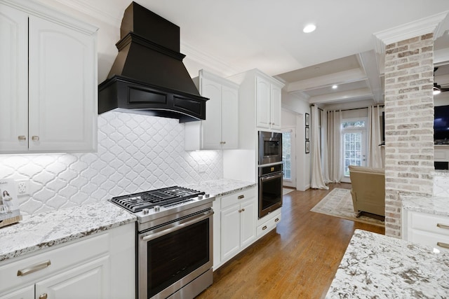 kitchen with beam ceiling, light wood finished floors, stainless steel appliances, white cabinets, and premium range hood