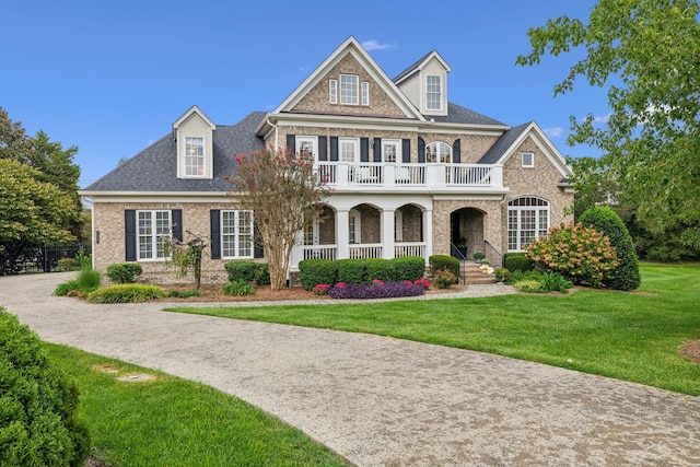 view of front of house featuring brick siding, roof with shingles, covered porch, a front yard, and a balcony