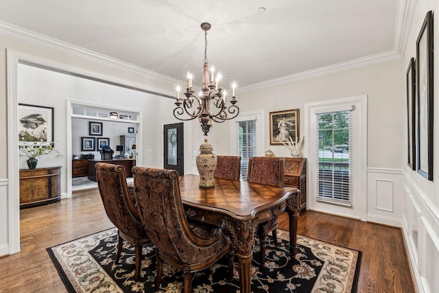 dining room with crown molding, a notable chandelier, a decorative wall, wainscoting, and wood finished floors