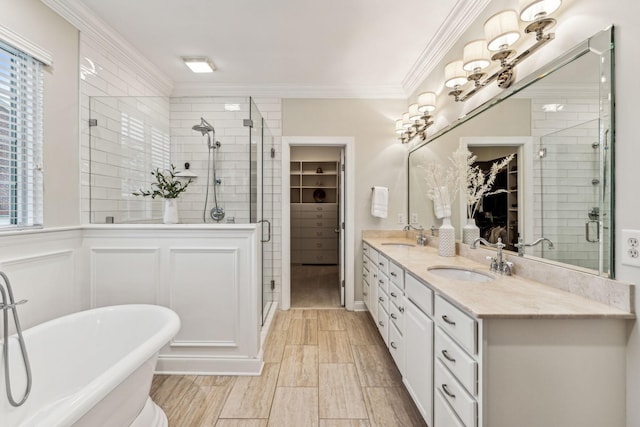 full bathroom with double vanity, a walk in closet, crown molding, a freestanding tub, and a sink